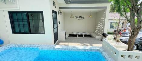 A swimming pool with a tiled deck, a covered seating area, and a wall with a sign.