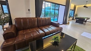 Un salon moderne avec un canapé en cuir, une table basse en verre et un billard.
