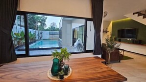 Un salon moderne avec une table basse en bois, un téléviseur et une vue sur une piscine.