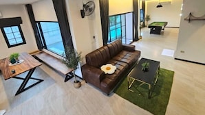 Un salon moderne avec un canapé en cuir, une table de billard et de grandes fenêtres.