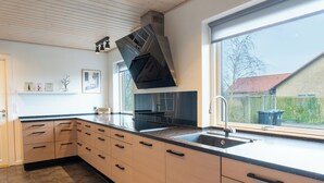 A modern kitchen with a large window, a built-in stove, and a sink. - Villa Holstebro (Holstebro)