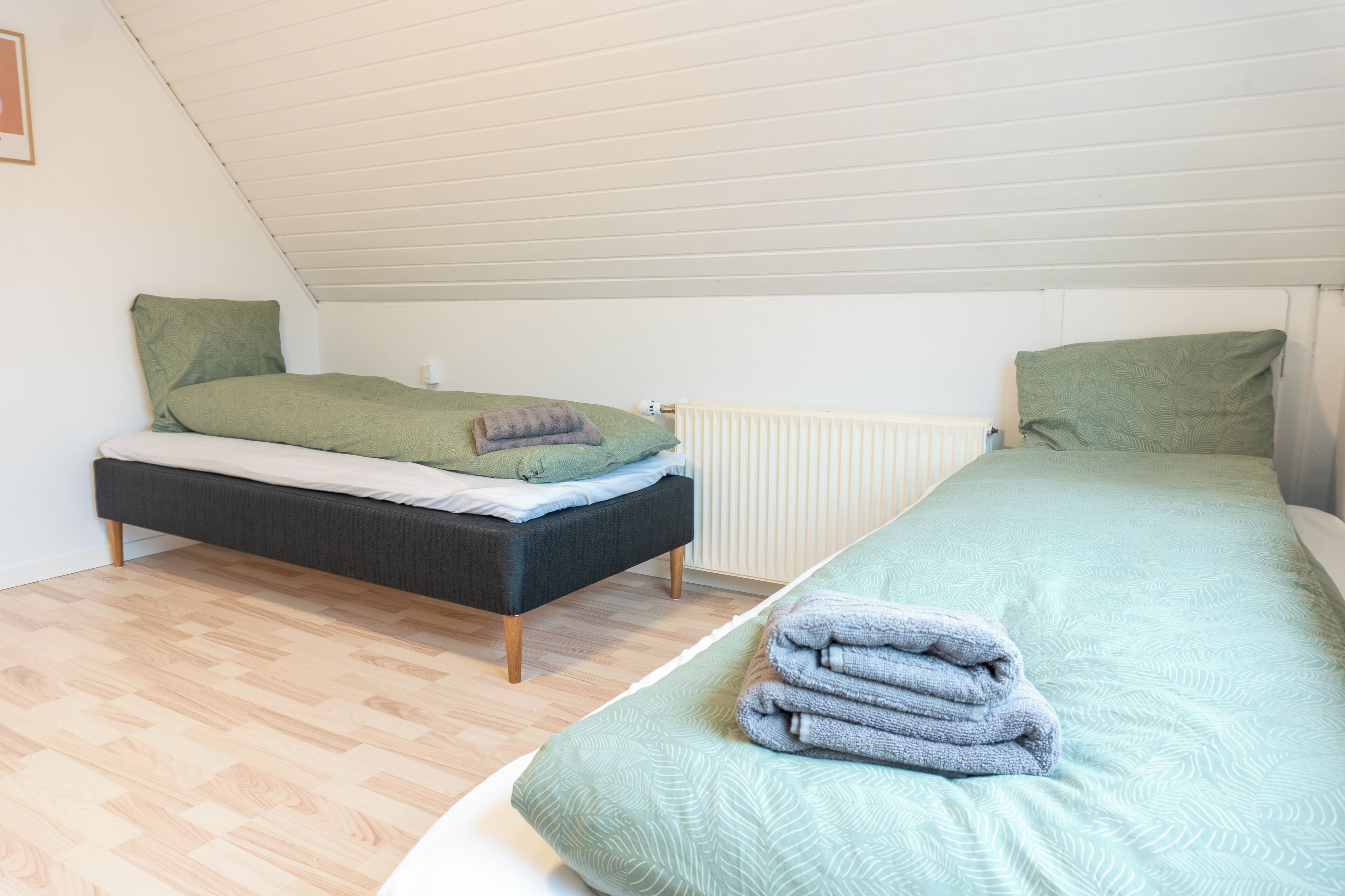 A bedroom with two beds, a radiator, and a wooden floor.