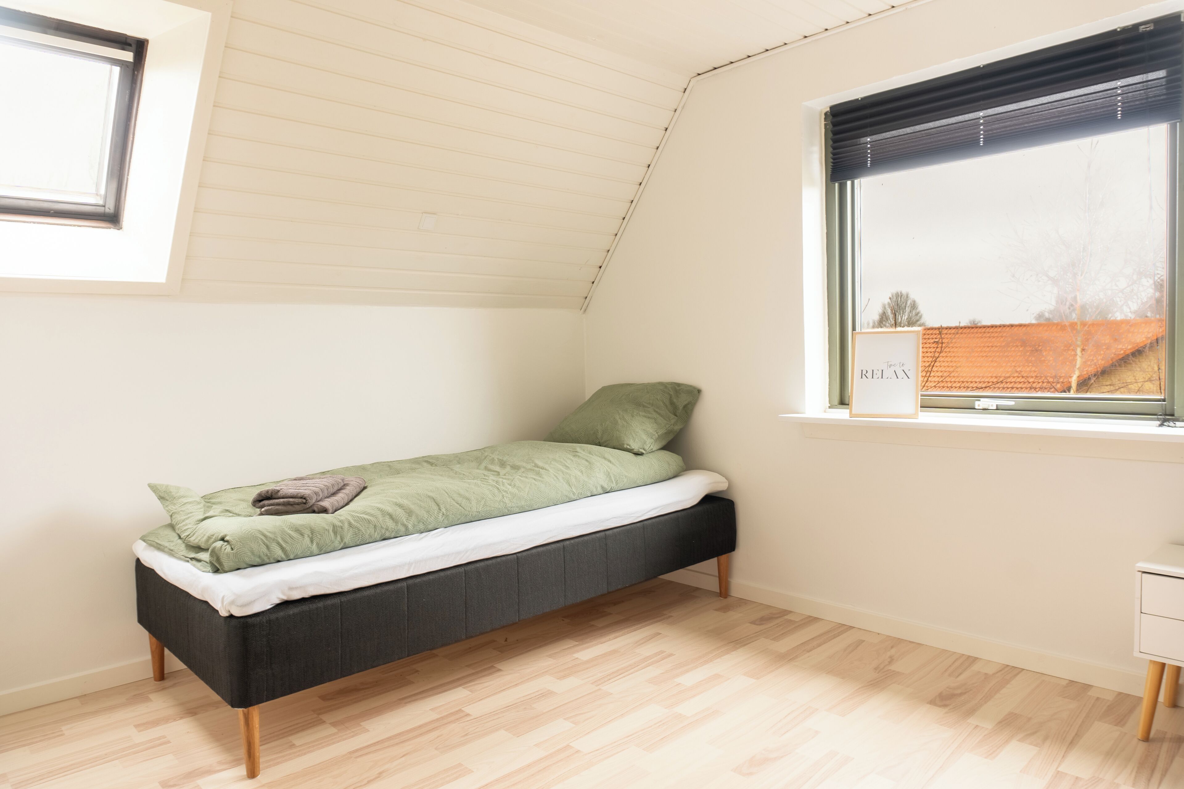 A small, single-bed room with a sloped ceiling and a window with blinds.