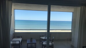 Ein Balkon mit Blick auf Strand und Meer. Zwei Stühle und ein kleiner Tisch mit einer Pflanze sind ebenfalls vorhanden.