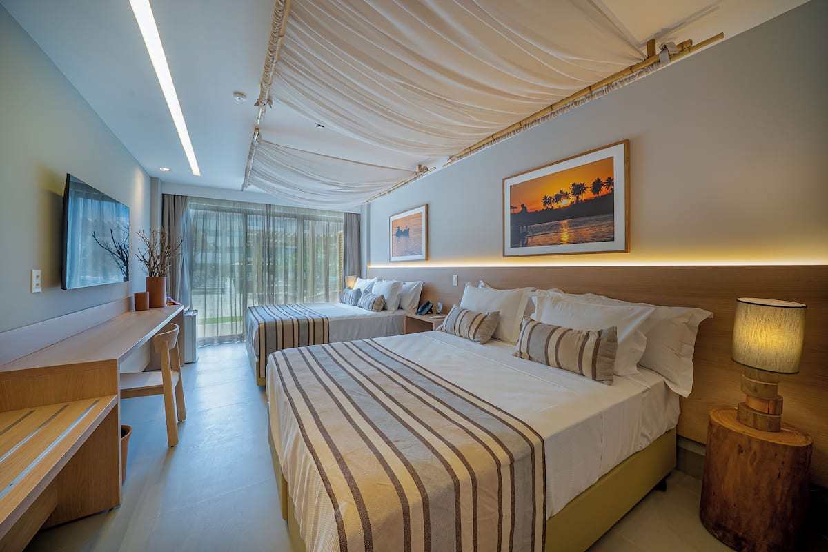 Une chambre d’hôtel avec deux lits, un bureau, une chaise, une lampe et une grande fenêtre avec des rideaux.