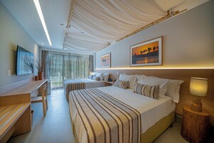Quarto de hotel com duas camas, uma mesa, uma cadeira, um abajur e uma janela grande com cortinas.