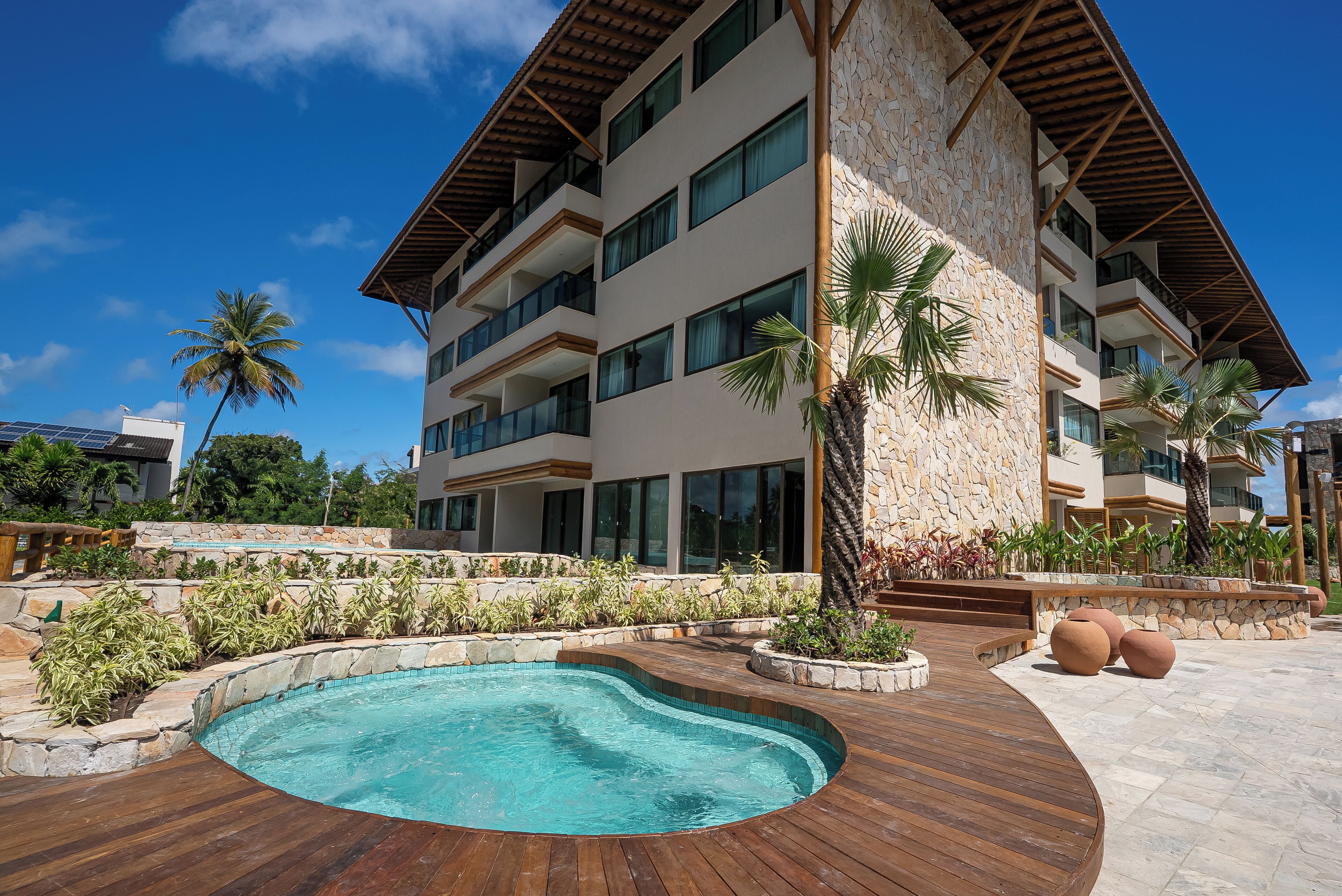 A modern hotel with a swimming pool, multiple balconies, and tropical landscaping.