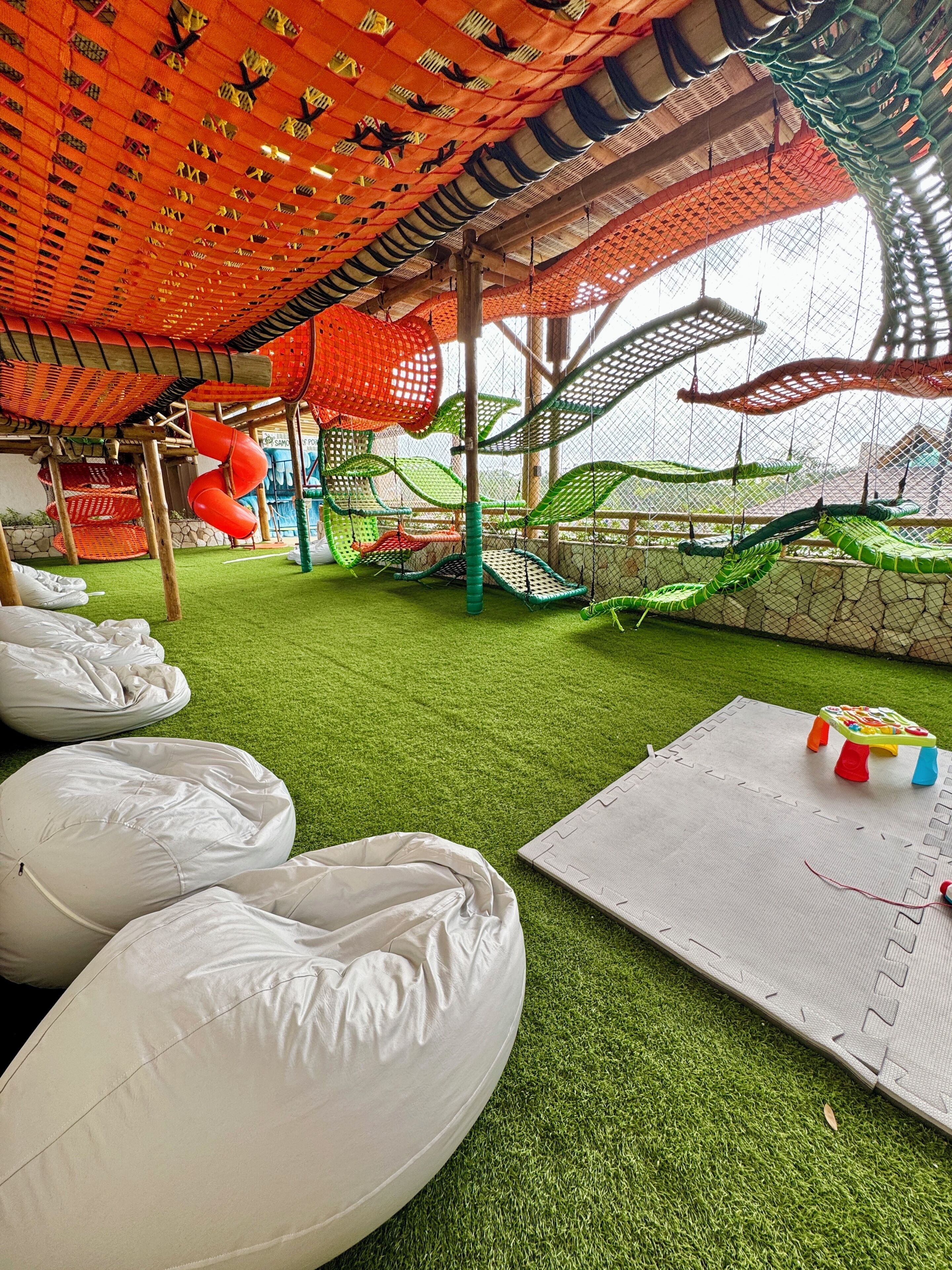 An indoor play area with artificial grass, hanging swings, and a climbing net structure.