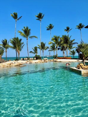 Une piscine d’eau cristalline, bordée de palmiers et d’une plage de sable fin.
