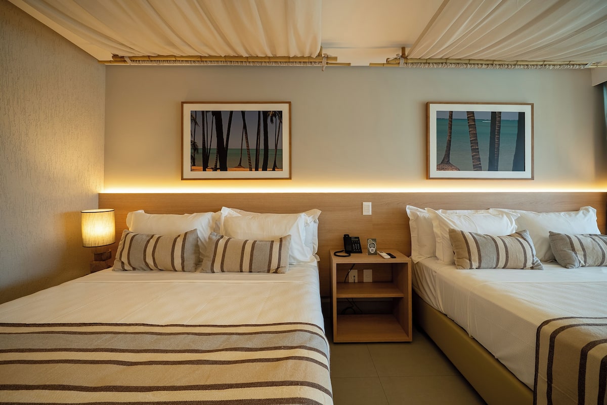Une chambre d’hôtel avec deux lits, une table de chevet avec une lampe et des œuvres d’art encadrées accrochées au mur.