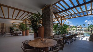 A spacious outdoor area with a round wooden table surrounded by wicker chairs, a stone pillar, and potted plants.