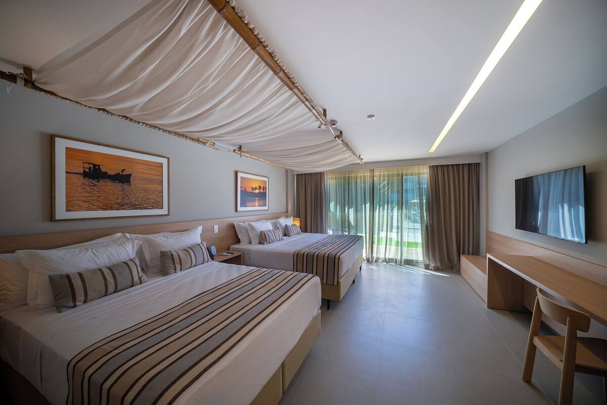 Une chambre d’hôtel avec deux lits, un bureau, une télévision et de grandes fenêtres avec des rideaux.