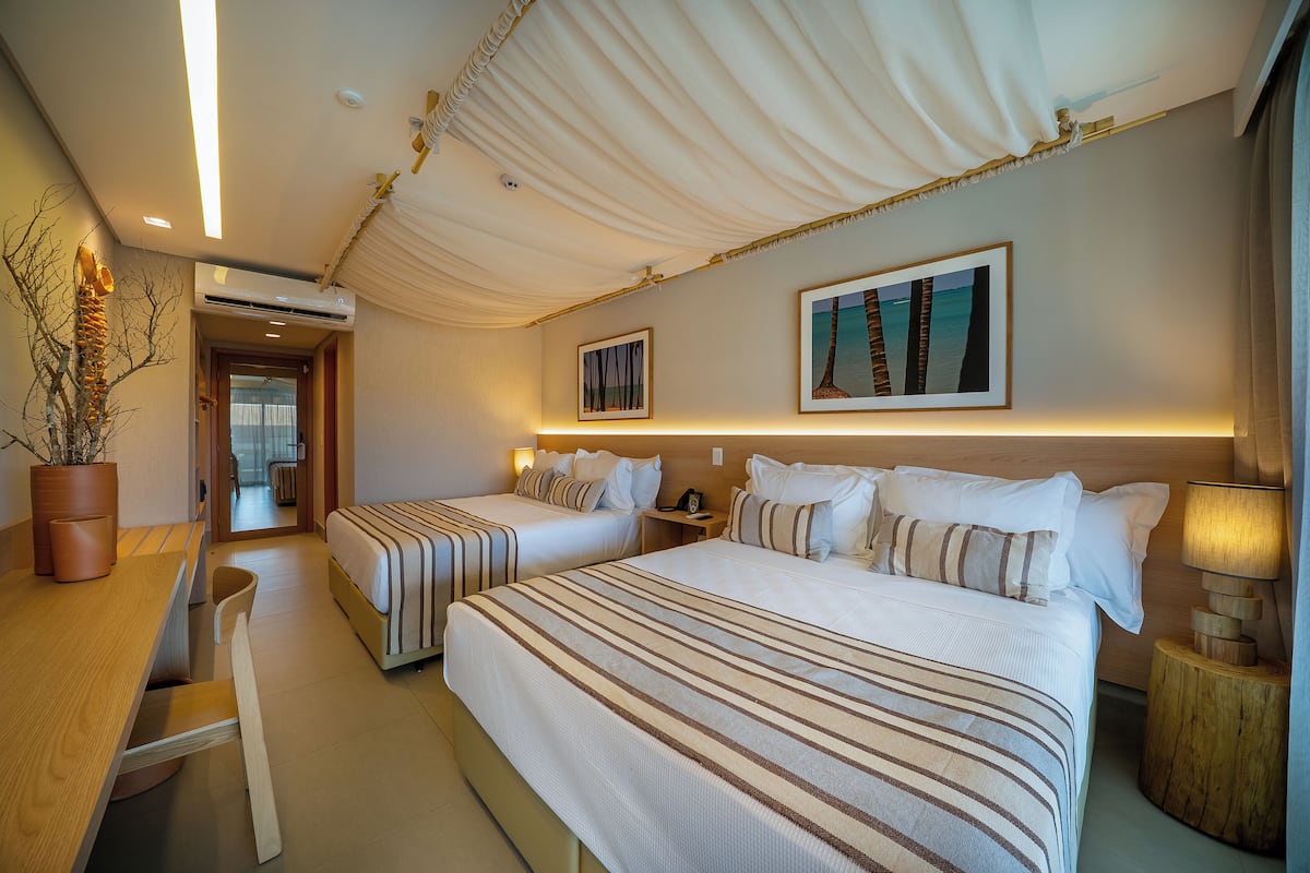Une chambre d’hôtel avec deux lits, un bureau en bois, une plante en pot et un plafond décoré de tissus drapés.