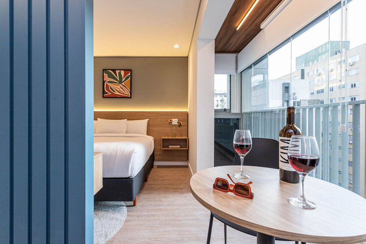 A modern hotel room with a bed, bedside table, and a balcony with a city view.