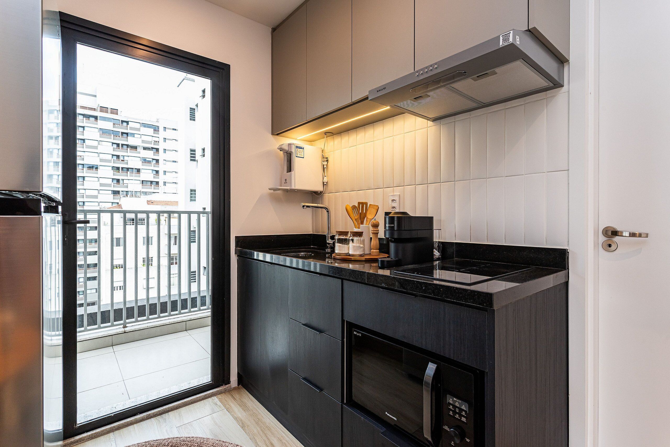 A modern kitchen with a built-in oven, a coffee maker, and a view of a balcony.