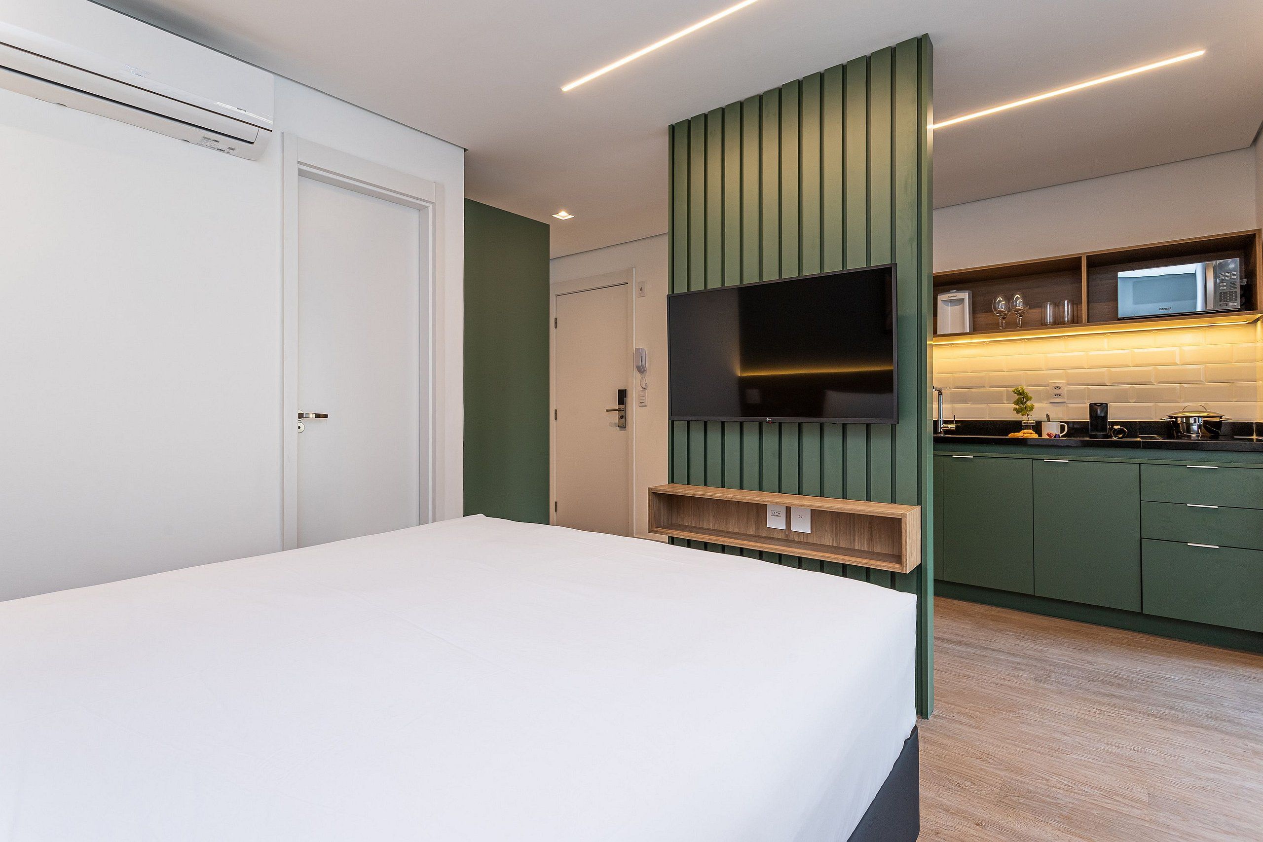 Una habitación de hotel moderna con una cama, un televisor, una kitchenette y una puerta.