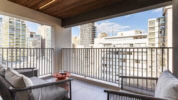 Un balcone con vista sugli edifici circostanti, un tavolo con una ciotola e occhiali da sole, e un divano.