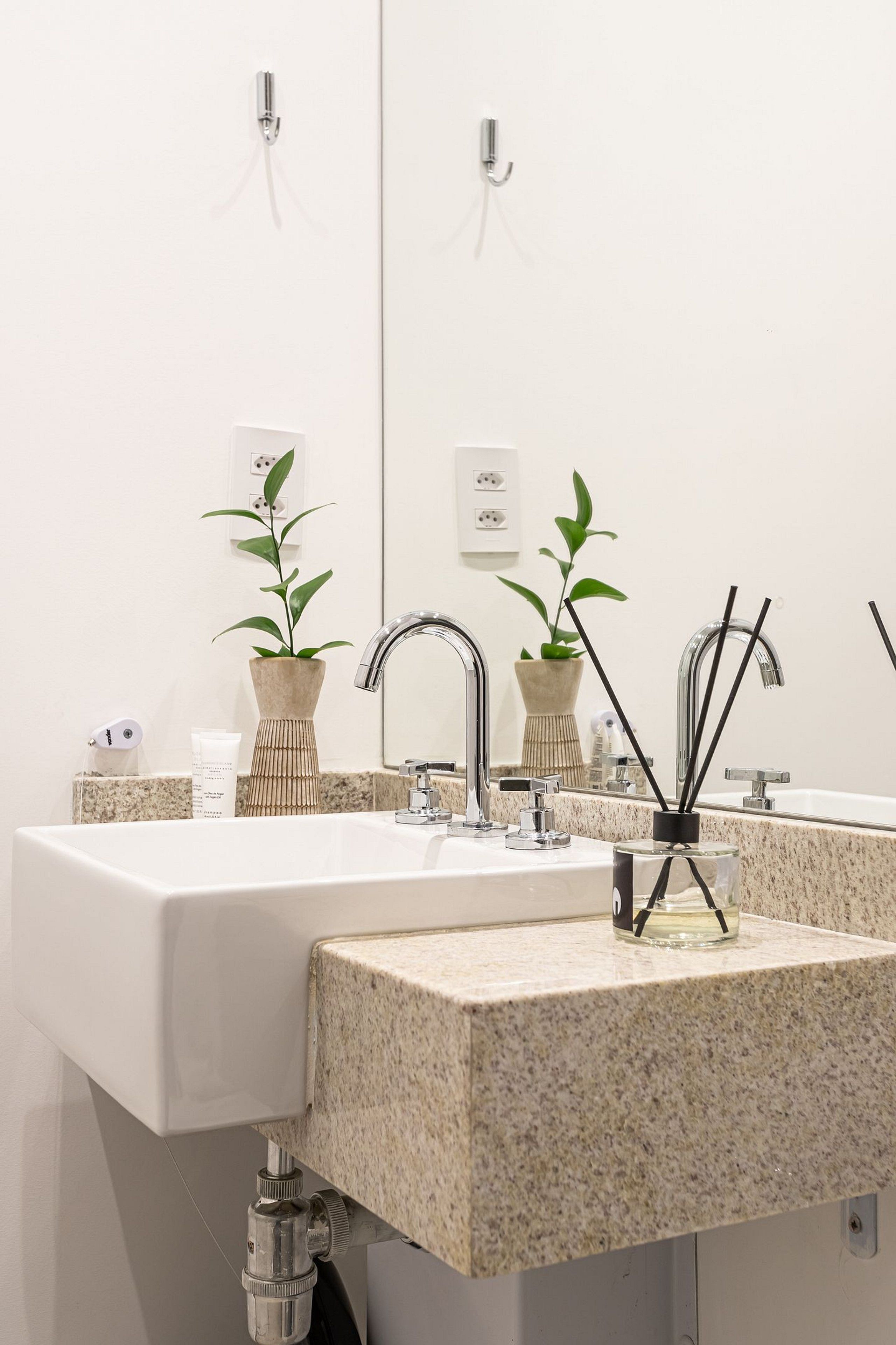 A bathroom with a white sink, two mirrors, and two potted plants.