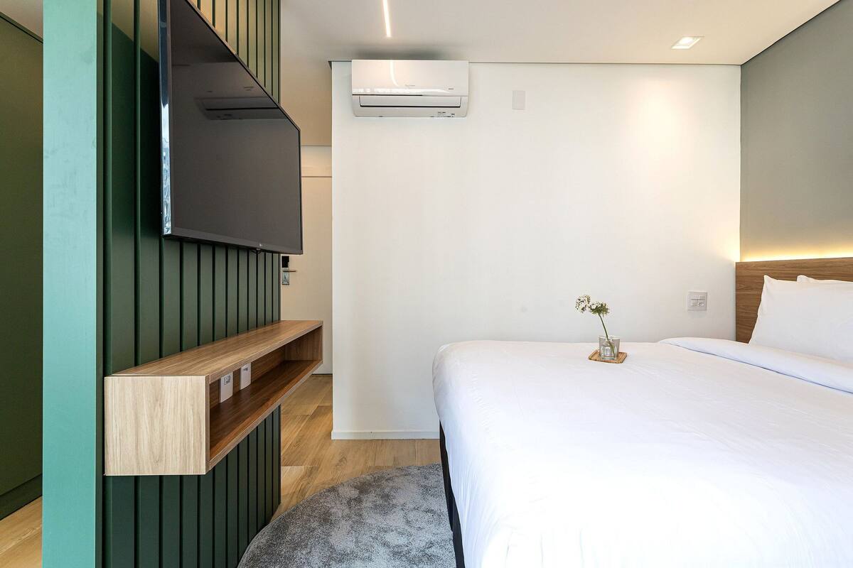 Une chambre d’hôtel moderne équipée d’un lit, d’un téléviseur fixé au mur, d’une étagère intégrée et d’un appareil de climatisation.