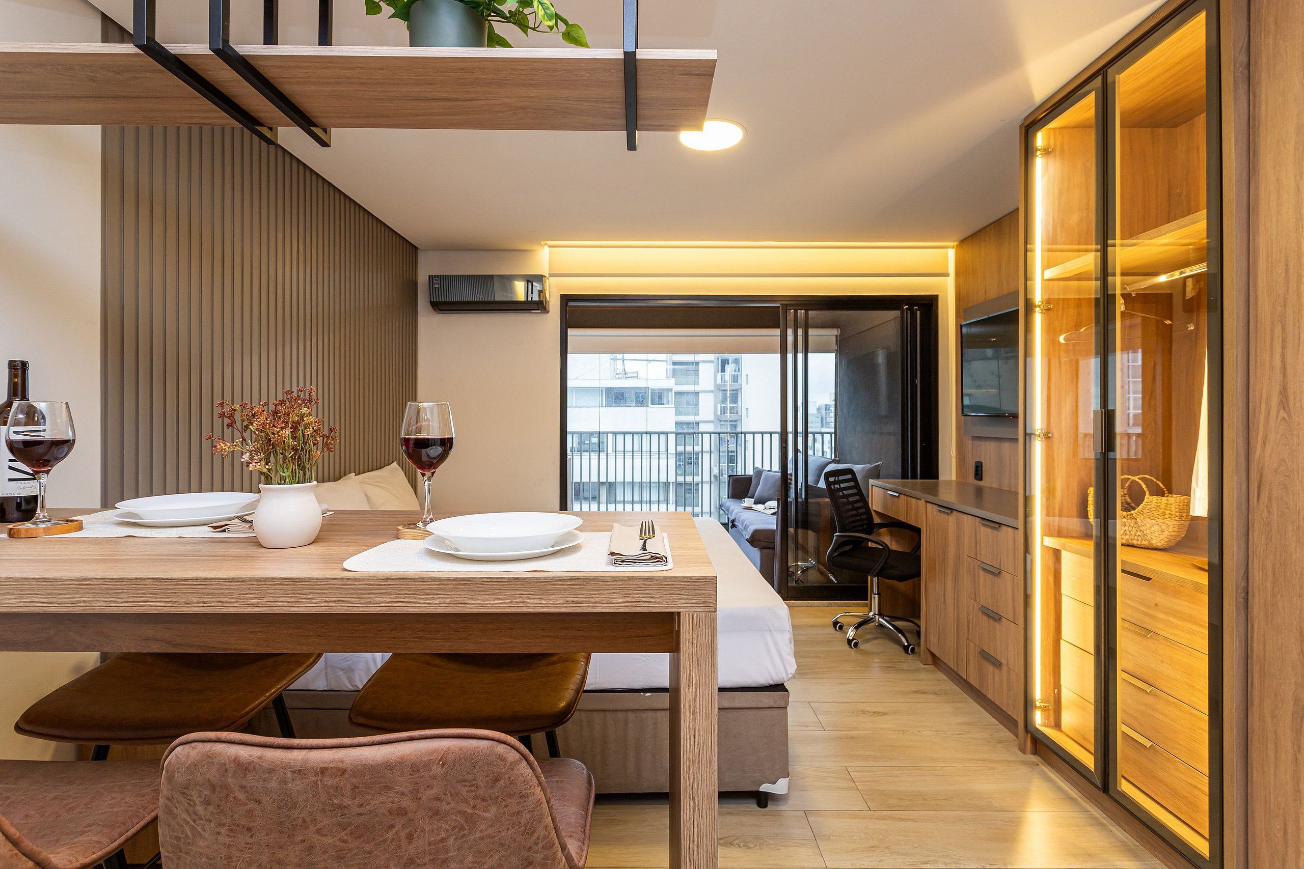 Un comedor moderno con una mesa de madera para dos personas, un sofá y una cocina con armarios de madera y horno empotrado.