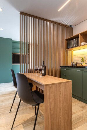 A modern kitchen with a wooden island, green cabinets, and a black chair. - Pivô Pamplona by Viva - Apartamentos novos e espaçosos ao lado da Av Paulista (São Paulo)