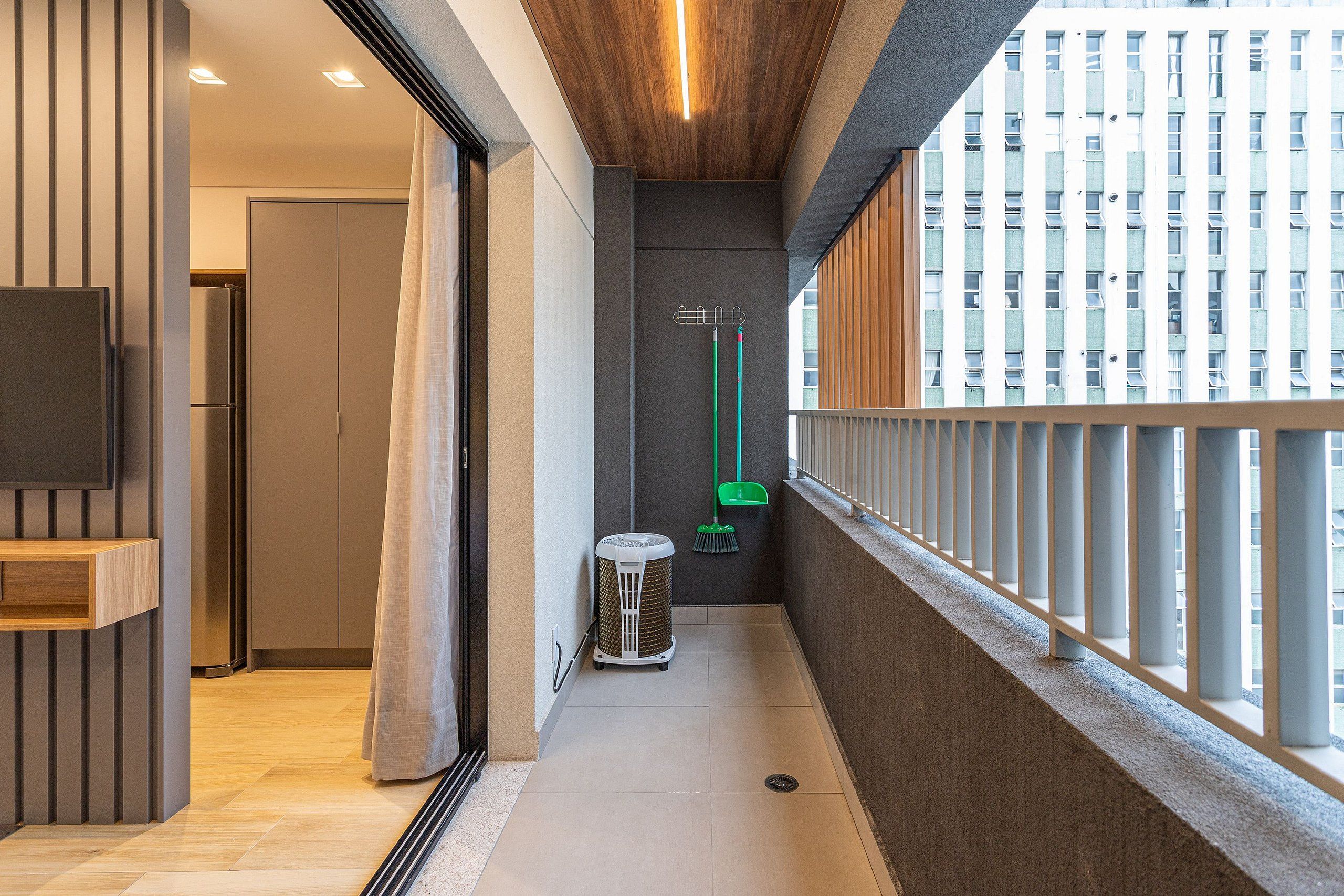 A narrow corridor with a wooden ceiling, a television mounted on the left wall, a trash bin, and a broom leaning against the wall.