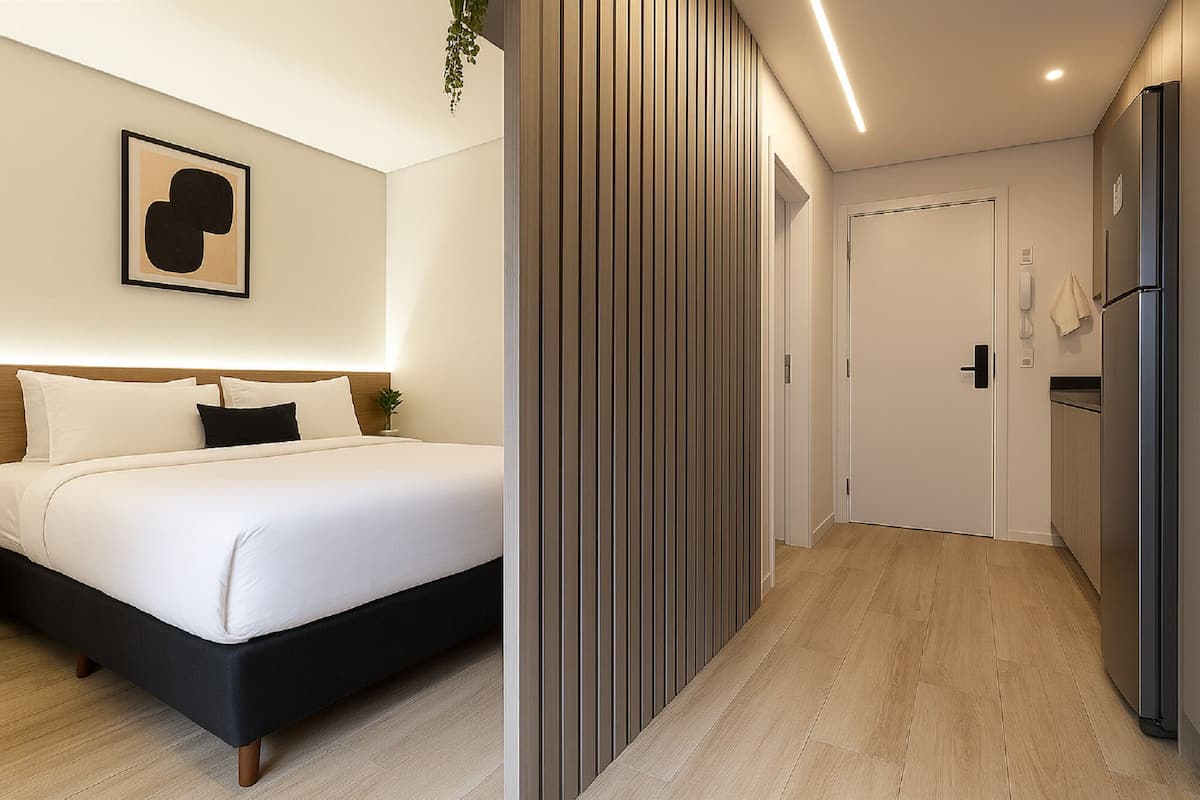 Une chambre d’hôtel moderne avec un lit, une œuvre d’art accrochée au mur, une plante et un couloir menant à une porte.