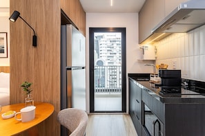 A modern kitchen with a built-in stove, a refrigerator, and a dining area with a table and chairs. - Pivô Pamplona by Viva - Apartamentos novos e espaçosos ao lado da Av Paulista (São Paulo)