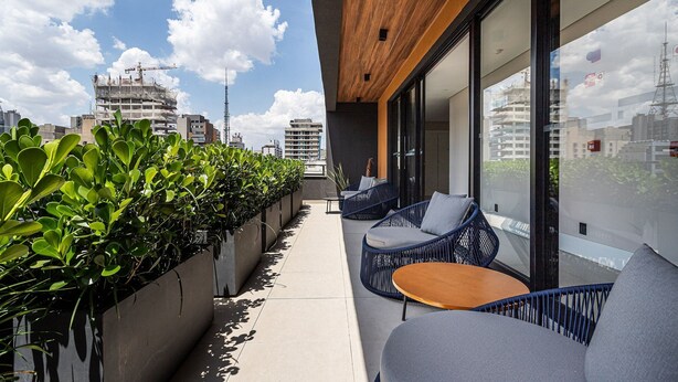 A balcony with seating, a planter with greenery, and a view of the cityscape. - Pivô Pamplona by Viva - Apartamentos novos e espaçosos ao lado da Av Paulista (São Paulo)