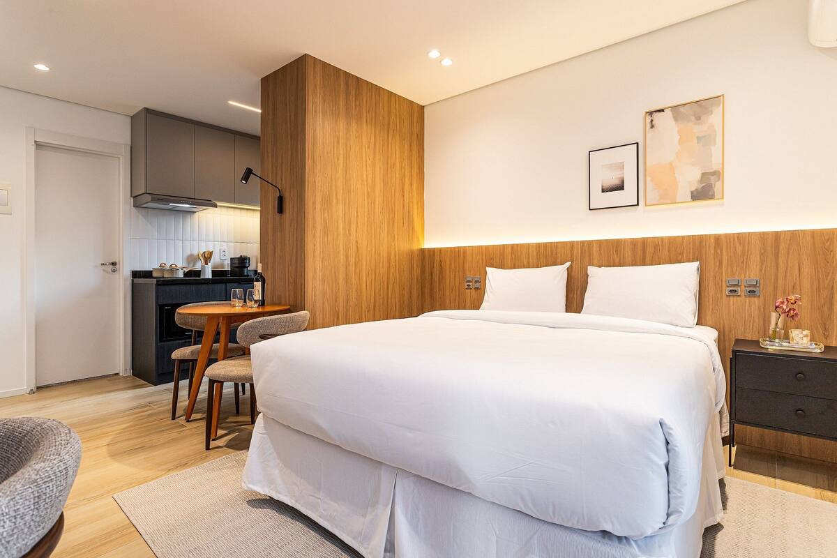 Une chambre d’hôtel moderne avec un grand lit, un coin repas et une cuisine en arrière-plan.