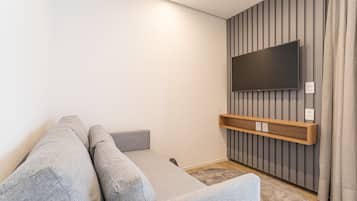 A modern living room with a grey sofa, a mounted TV, and a wooden shelf.