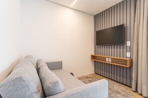 A modern living room with a grey sofa, a mounted TV, and a wooden shelf. - Pivô Pamplona by Viva - Apartamentos novos e espaçosos ao lado da Av Paulista (São Paulo)
