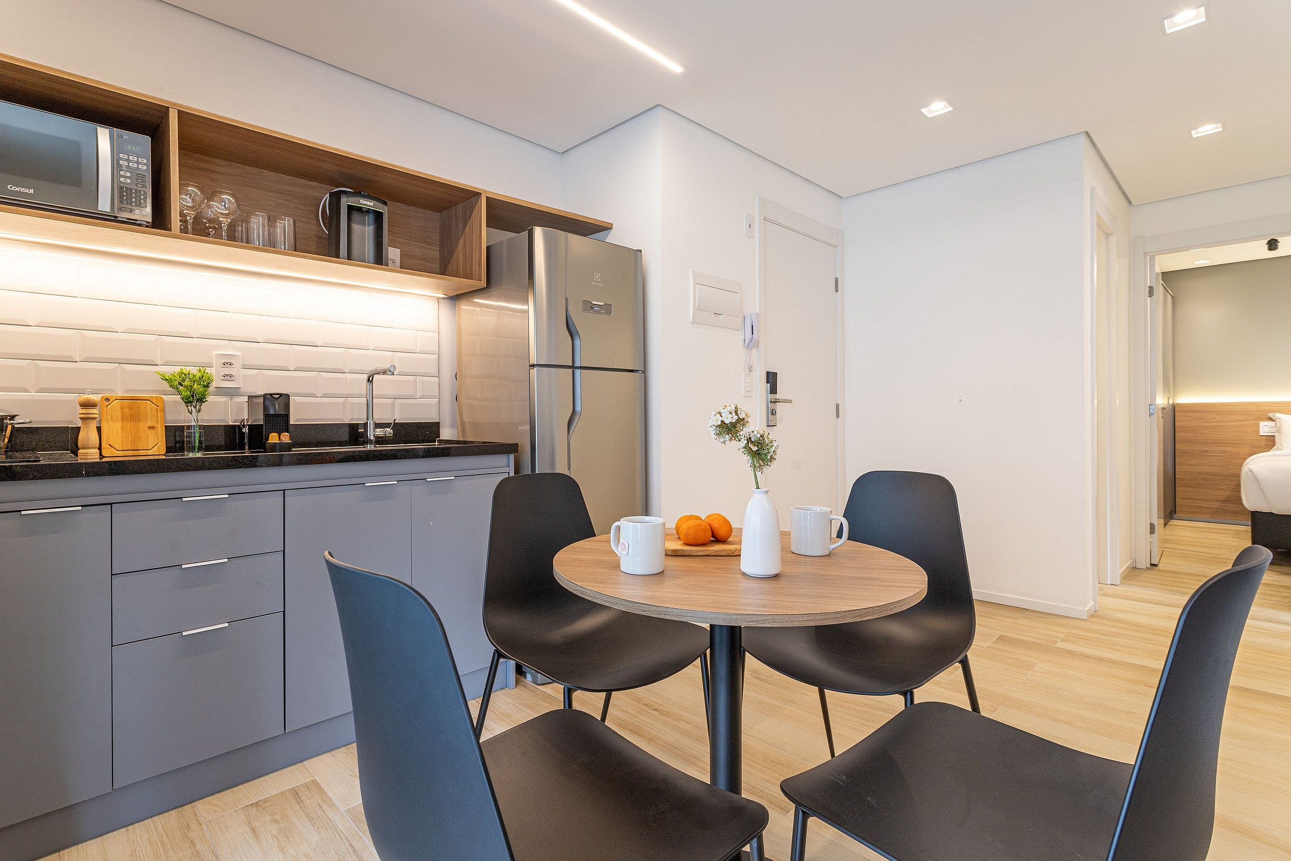 A modern kitchen with grey cabinets, a built-in microwave, and a stainless steel refrigerator.