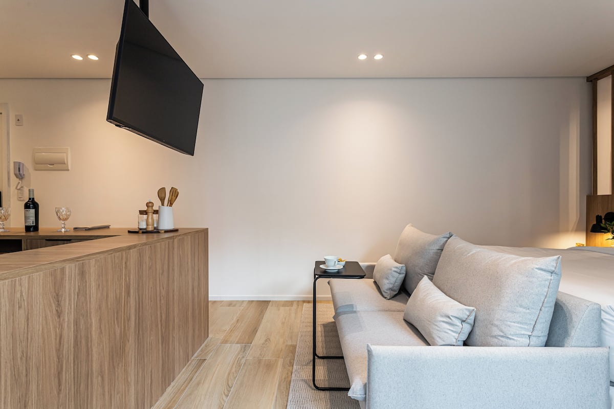Une chambre d’hôtel moderne avec un comptoir d’accueil en bois, un canapé, une petite table avec une tasse et un téléviseur à écran plat fixé au mur.