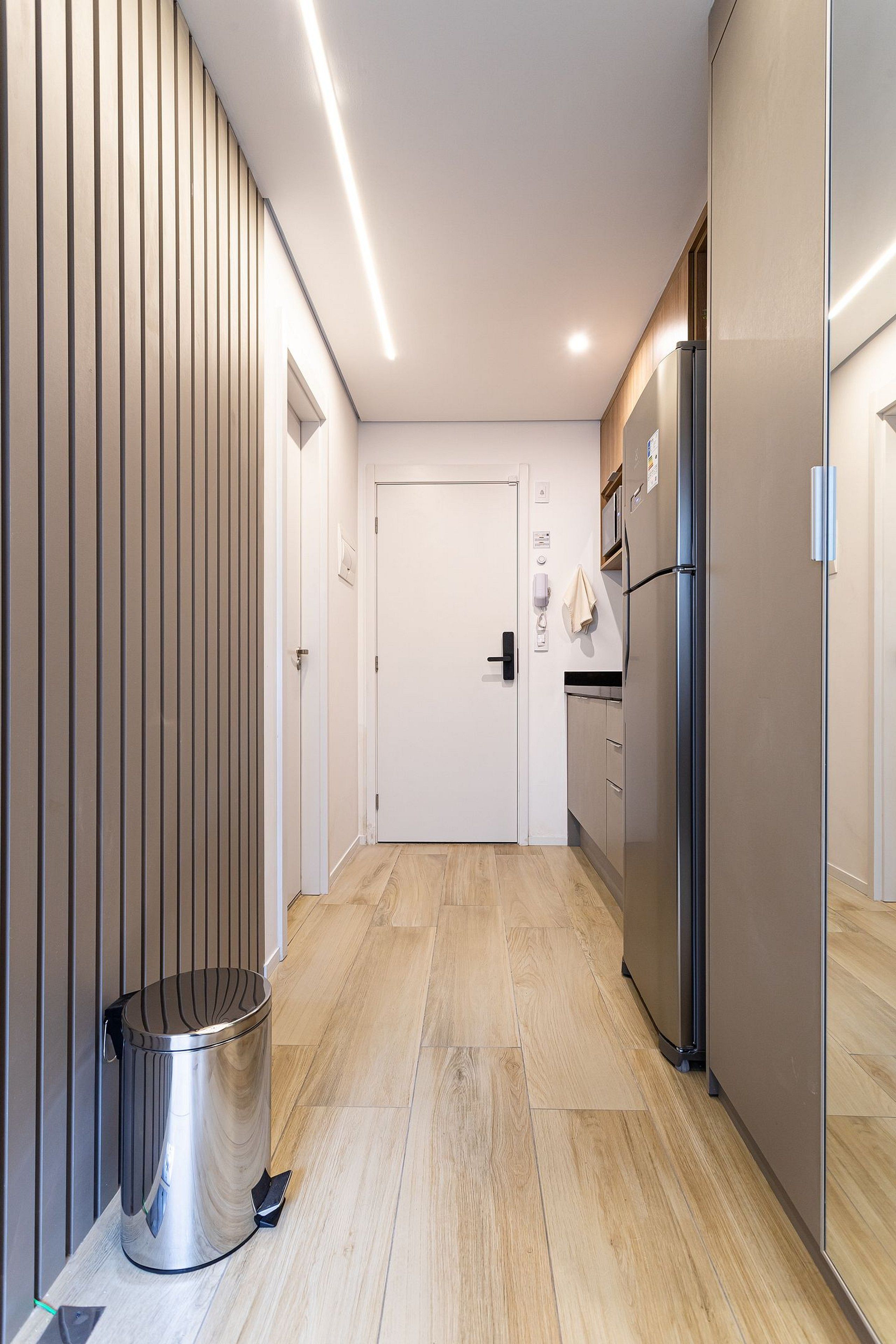 A modern kitchen with a stainless steel refrigerator, wooden flooring, and a trash bin.