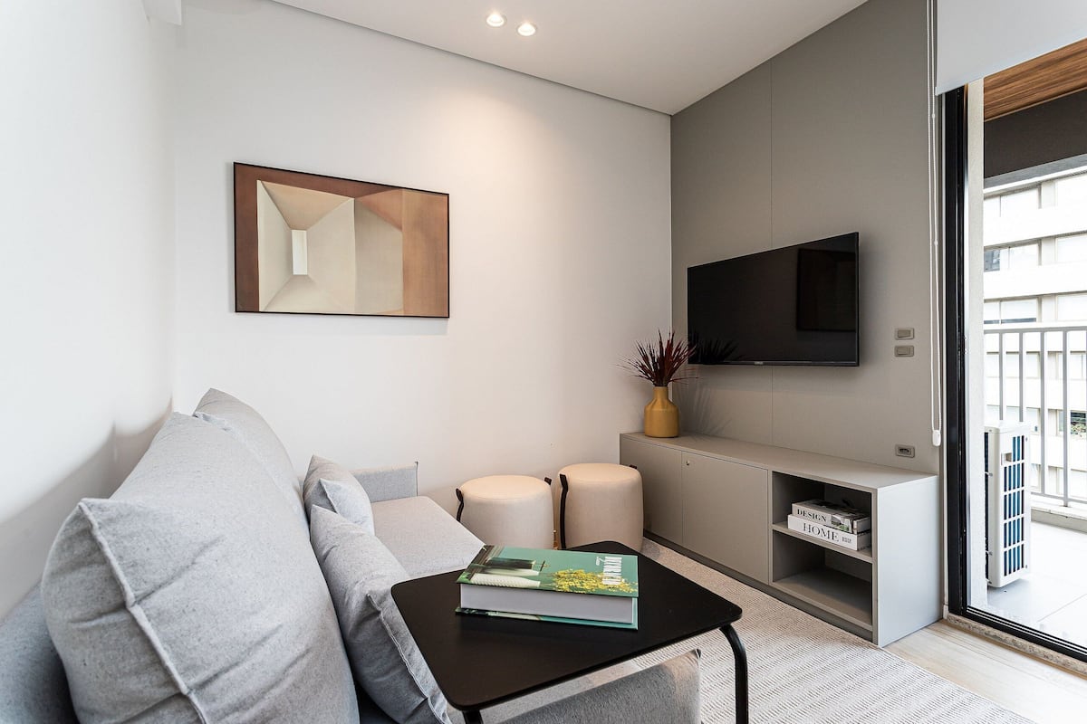 Un salon moderne avec un canapé, une table basse sur laquelle repose un livre, un téléviseur à écran plat et une décoration minimaliste.