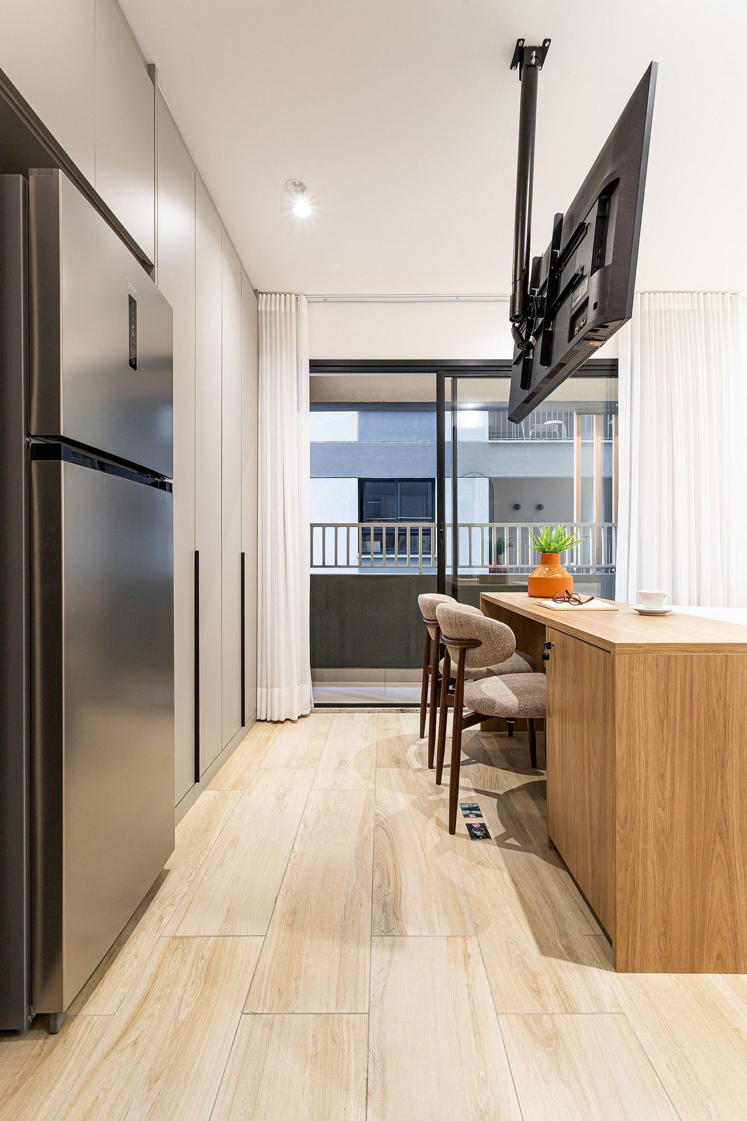 Une cuisine moderne dotée d’un réfrigérateur encastré, d’un îlot central en bois et d’une grande fenêtre offrant une vue sur l’extérieur.