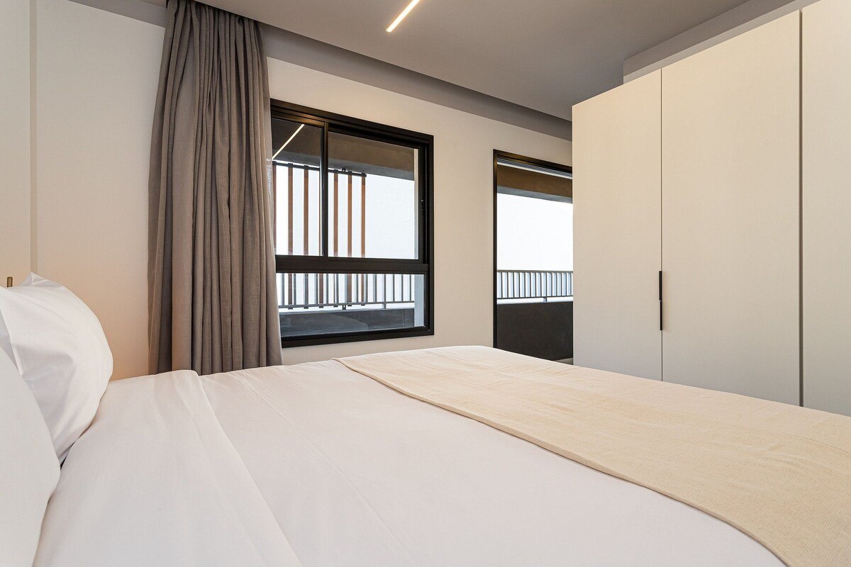 A hotel room with a bed, a window with a view of a balcony, and a wardrobe.