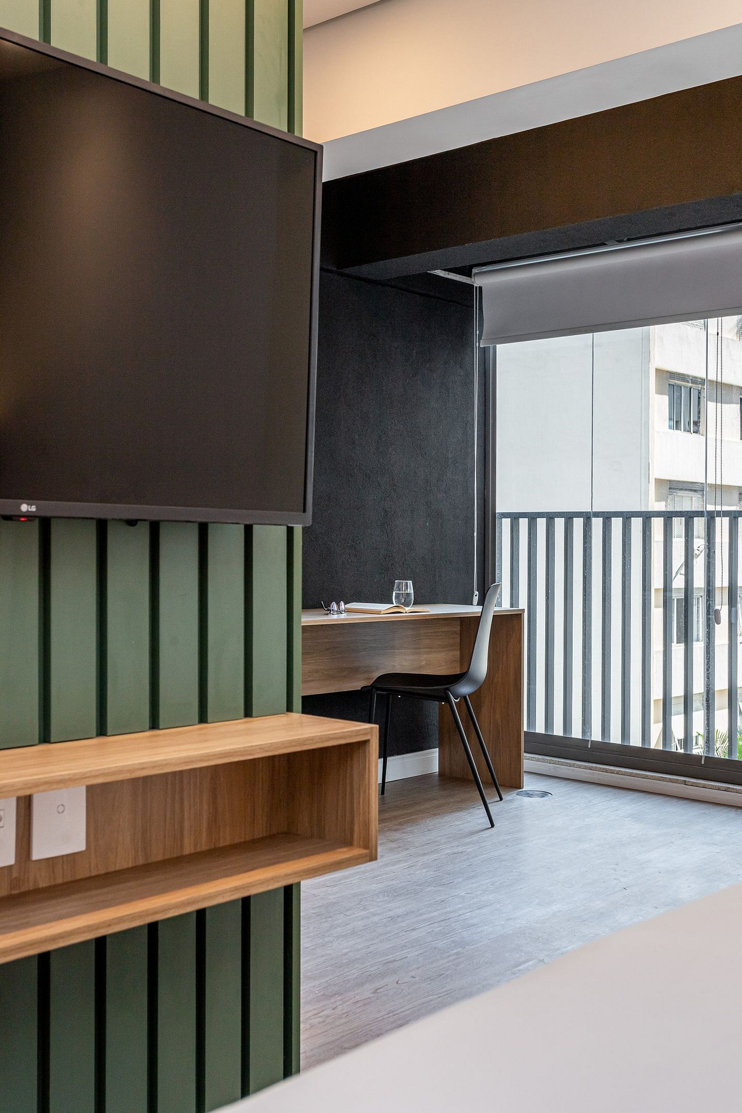 A modern room with a large flat-screen TV, a wooden desk, a chair, and a balcony with a railing.