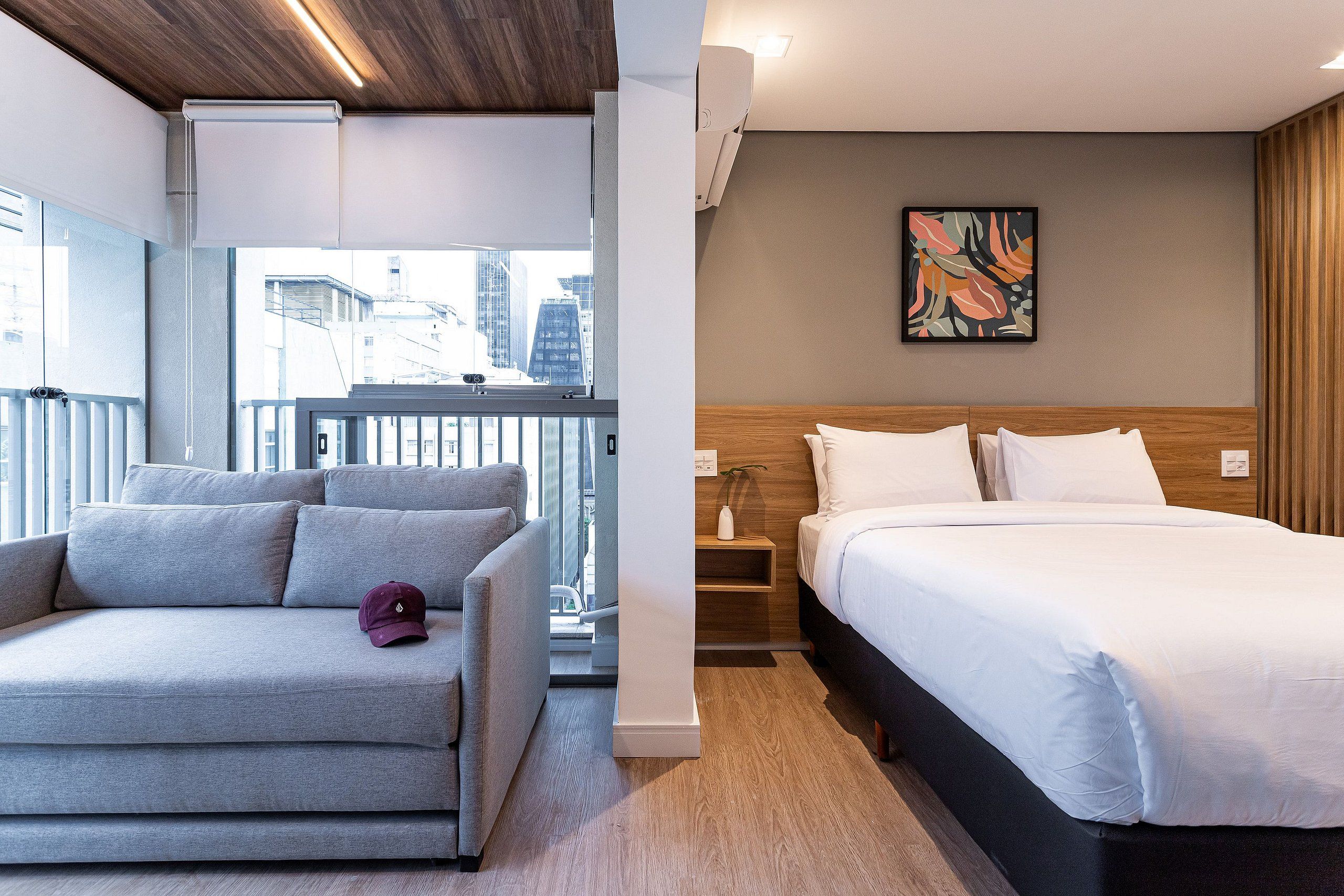 A modern hotel room with a bed, a sofa, a small table, and a window with a city view.