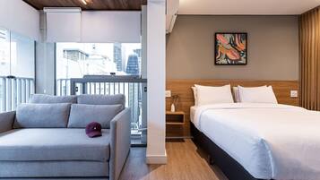 Una habitación de hotel moderna con una cama, un sofá, una mesita y un ventanal con vistas a la ciudad.