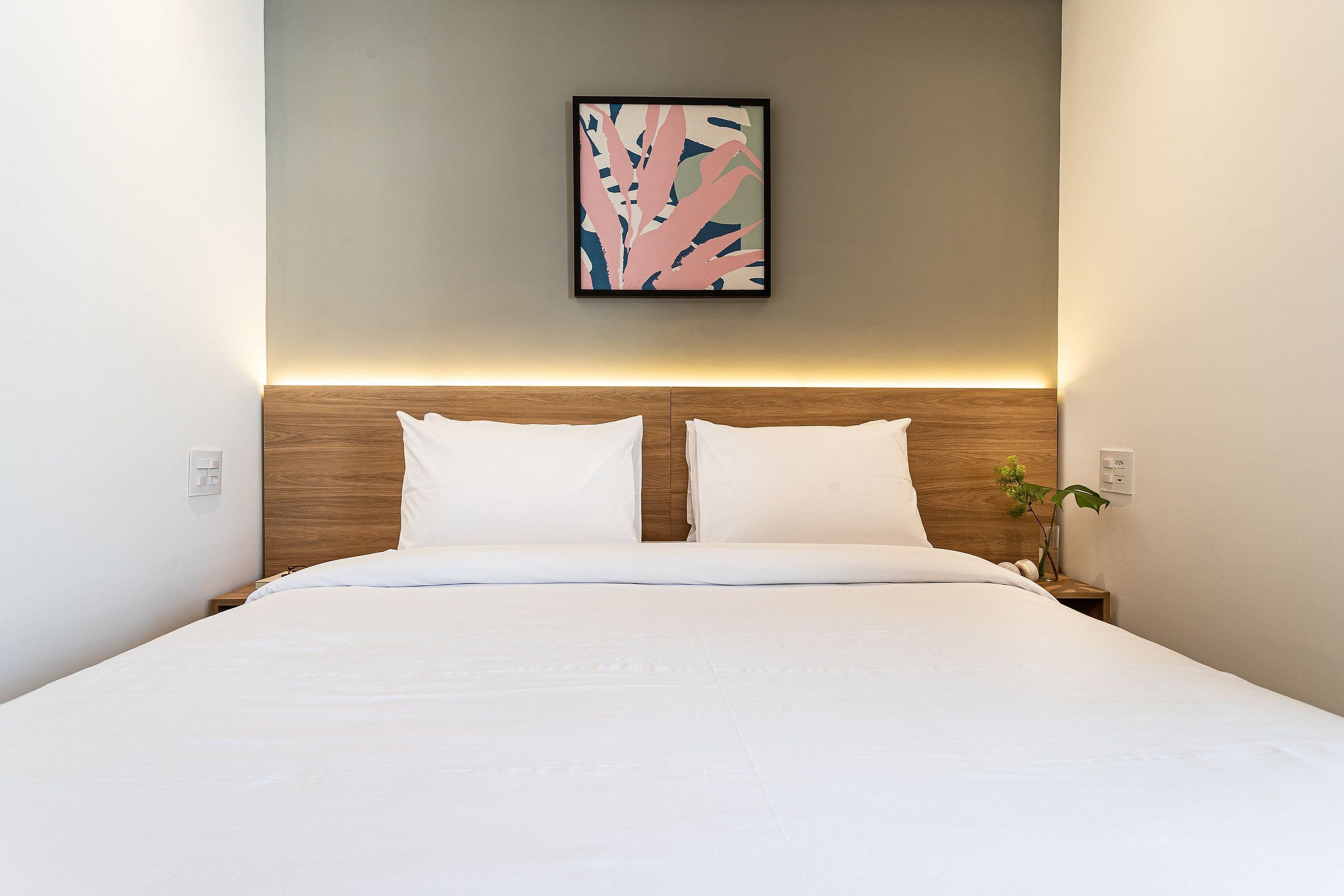 Ein ordentlich bezogenes Bett mit weißen Leinen, einem Holzkopfteil und einem an der Wand hängenden abstrakten Kunstwerk.