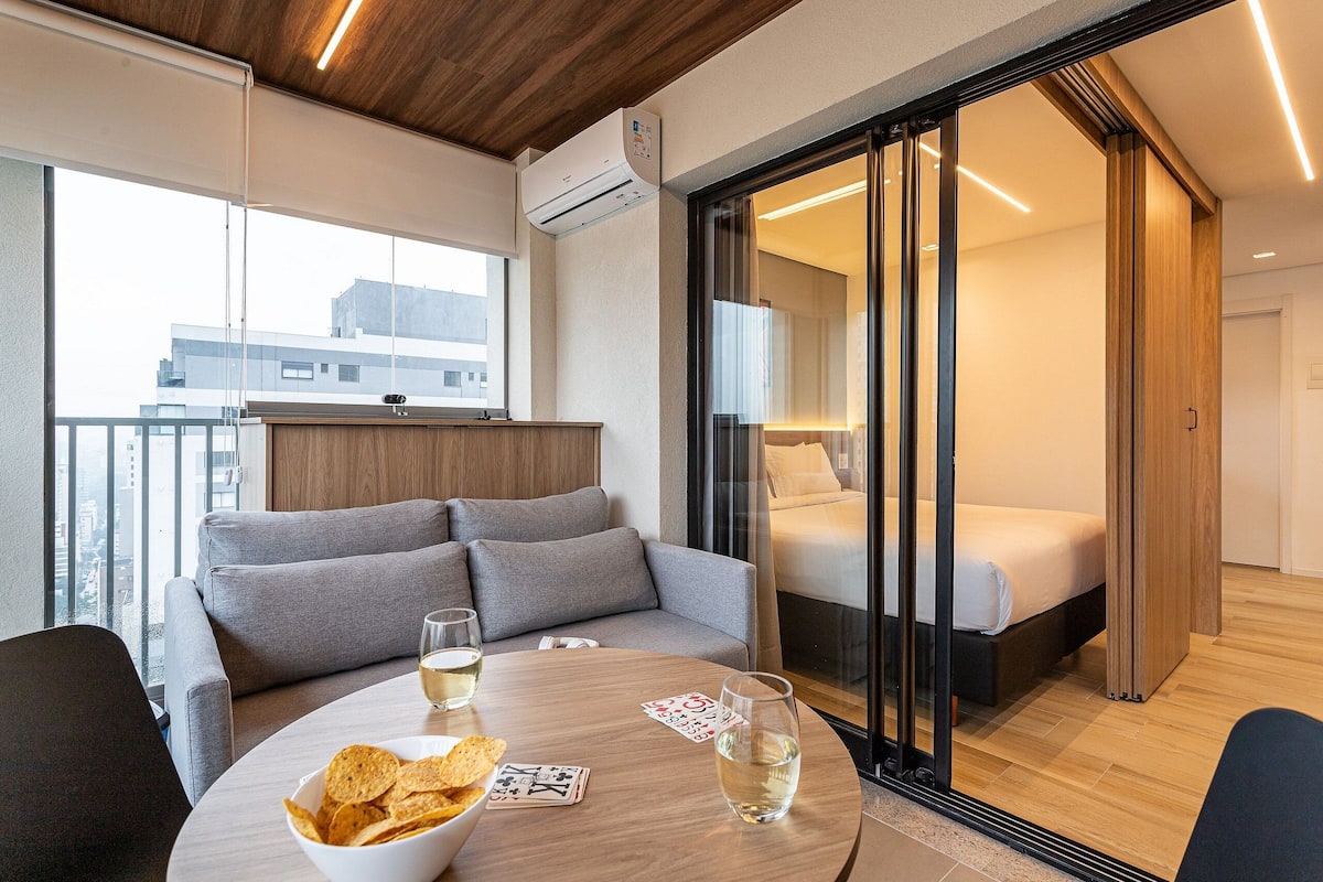 Une chambre d’hôtel moderne dotée d’un balcon, d’un canapé, d’une table ronde avec des collations et des boissons, et d’un lit avec une porte-fenêtre coulissante.