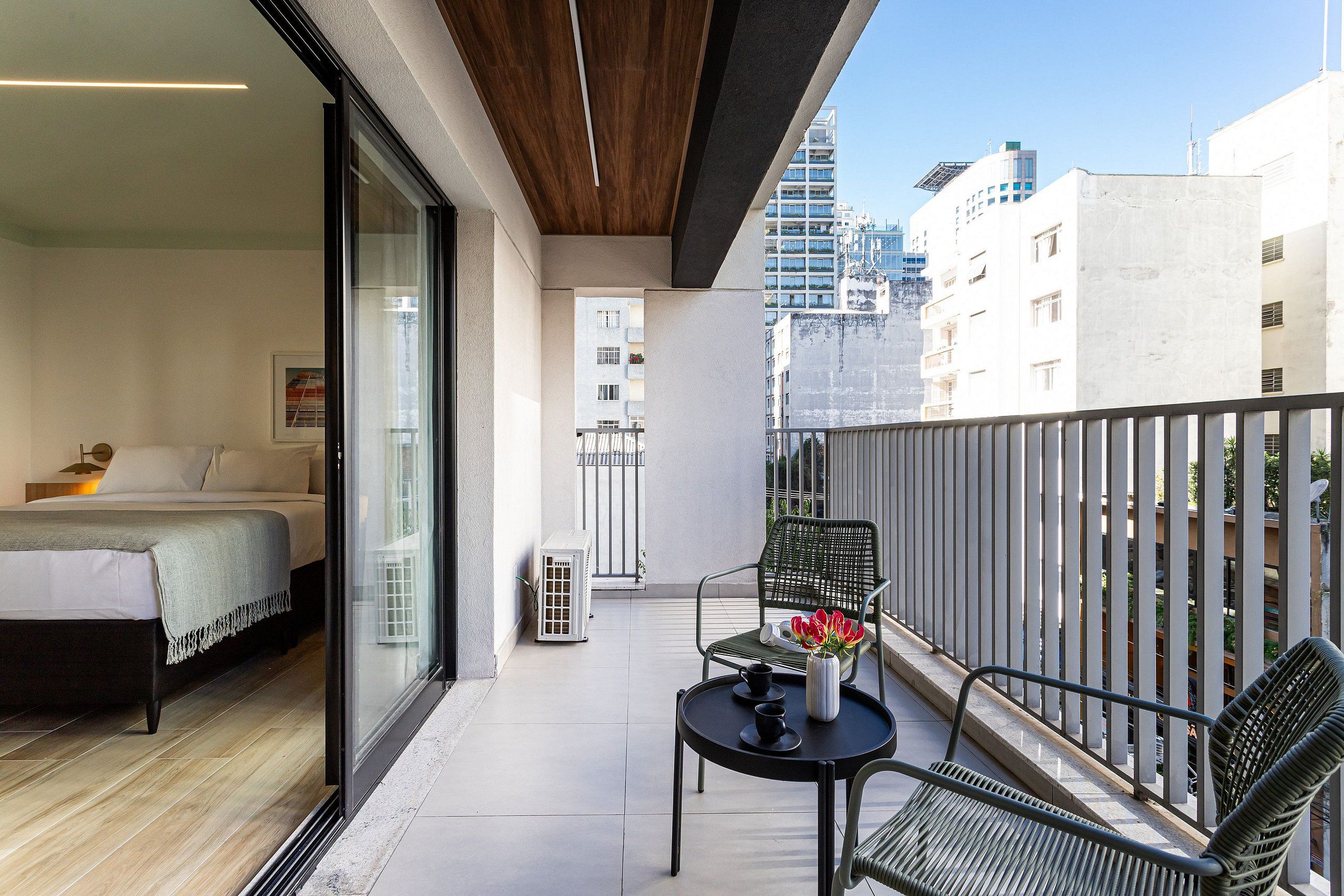 A balcony with a bed, a chair, and a table with a vase of flowers.