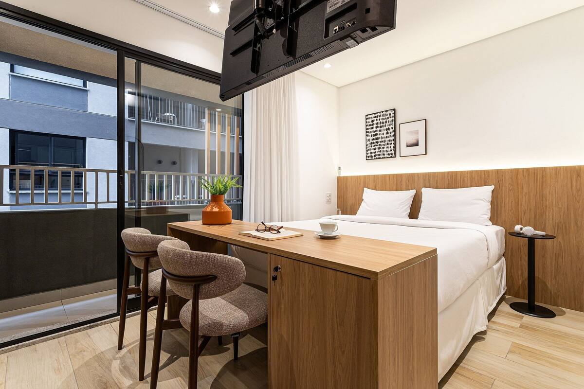 Une chambre d’hôtel avec un lit, un bureau avec des chaises, une télévision et une vue sur l’extérieur.