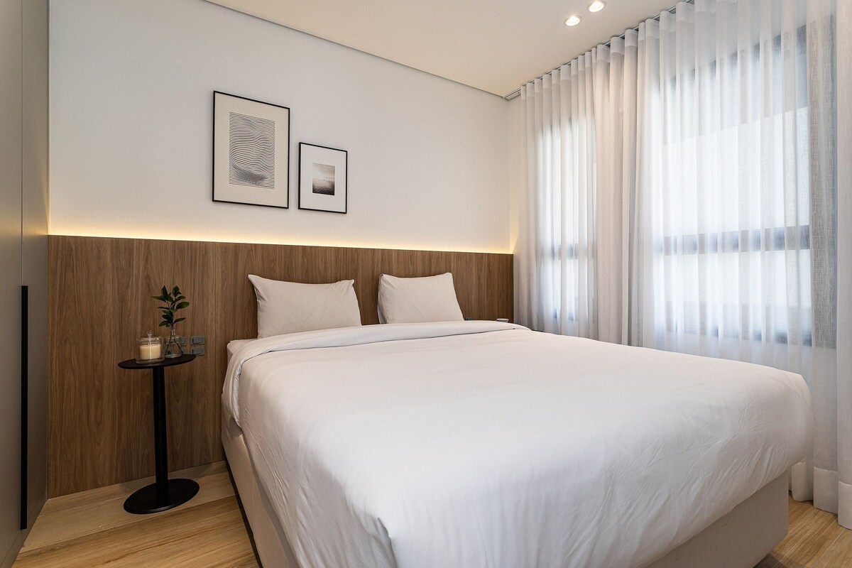 A modern hotel room with a large bed, a bedside table with a candle, and a wall-mounted picture.