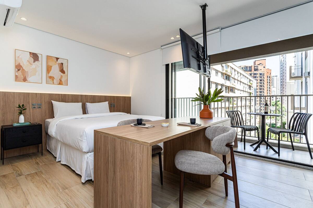 Une chambre d’hôtel moderne équipée d’un lit, d’un bureau et d’un balcon avec des chaises.
