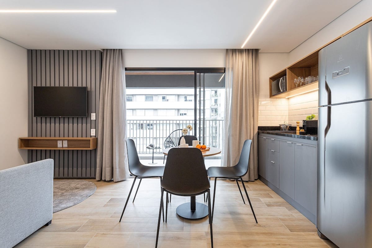 Une cuisine moderne dotée d’un réfrigérateur encastré, d’un coin repas avec deux chaises, d’un téléviseur à écran plat fixé au mur et offrant une vue sur la ville grâce à de grandes fenêtres.