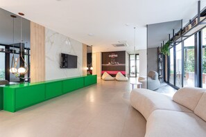A modern reception area with a green counter, a coffee station, and a large window offering a view of the outdoors. - Pivô Pamplona by Viva - Apartamentos novos e espaçosos ao lado da Av Paulista (São Paulo)