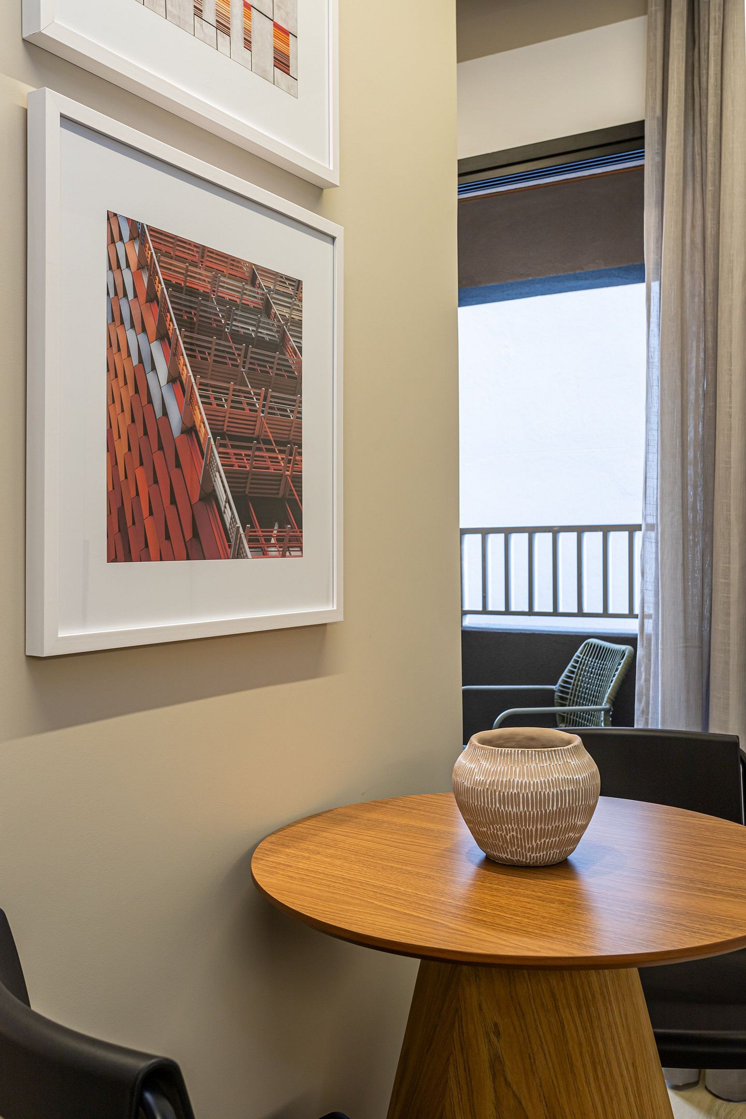 Ein Zimmer mit einem runden Holztisch, einer Vase und zwei gerahmten abstrakten Kunstwerken an der Wand.